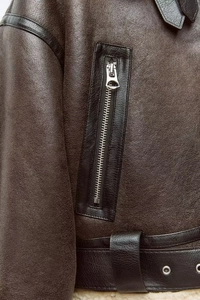 Detail view of dark brown shearling jacket featuring silver zippers and leather belt texture