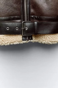 Detailed view of brown leather jacket hem with white fleece lining and belted buckle detail