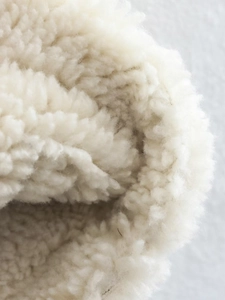 Macro shot of thick cream faux shearling lining showing dense fleece texture and warmth