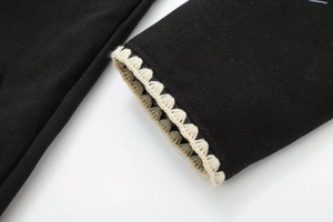 Detail of black wool coat cuff with contrast white embroidered wavy trim and neat stitching