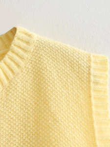 Detail of light yellow knit vest showing ribbed neckline and chunky knit texture fabric