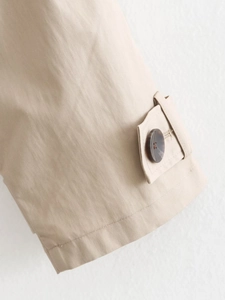 Detail of shoulder epaulet and marble button on beige slim fit trench coat fabric