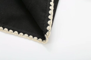 Close-up of white scallop crochet embroidery on black wool coat fabric edges