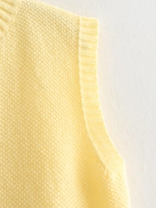 Close-up of the ribbed crewneck and armhole detail on a soft pale yellow knit vest
