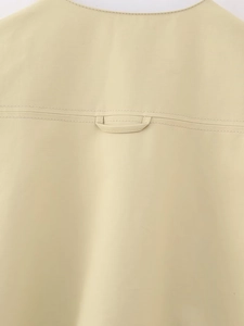 Detail of light yellow vest back showing fabric texture, hanging loop and double stitching