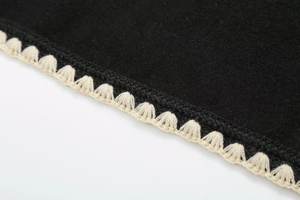 Detail of wool coat edge with premium off-white crochet knit trim on black fabric