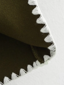 Macro shot of dark olive green knit fabric with decorative white whipstitch edge detail