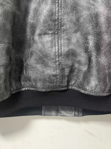 Close-up of the vintage distressed PU leather texture and ribbed hem on the biker jacket