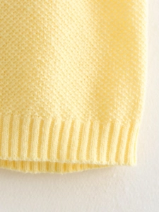 Detail of light yellow knit vest showing honeycomb texture and ribbed hem construction