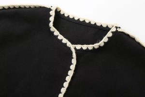 Detail of black wool coat featuring white crochet lace trim and textured fabric