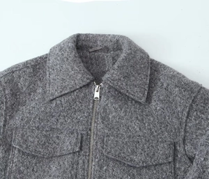 Detail of grey wool-like tweed jacket showing metal zipper and symmetrical chest pockets