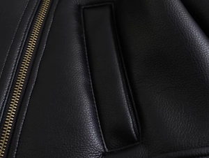 Détail d'une veste en cuir noir avec fermeture éclair en métal doré et grain de cuir