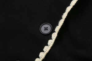 Detail view of black wool coat featuring a vintage button and ivory crochet lace trim