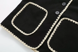 Detail of tweed coat featuring contrast crochet trim and decorative round black buttons