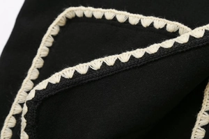 Close-up of contrast crochet lace trim on black wool coat showing stitching detail