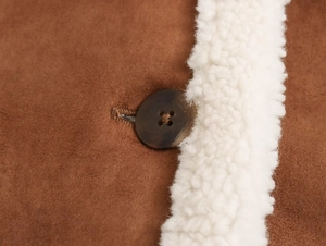 Macro shot of marble-pattern button on brown faux suede jacket with white shearling trim