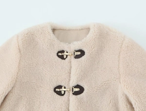 Detail of off-white faux fur jacket featuring metal snap buckles and leather trim details