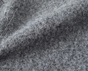 Close-up detail of grey bouclé tweed fabric texture with soft curly wool finish