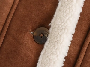Detailed close-up of brown suede fabric with white sherpa trim and textured round button