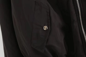 Close-up of black bomber jacket fabric showing a silver metal snap button and zipper