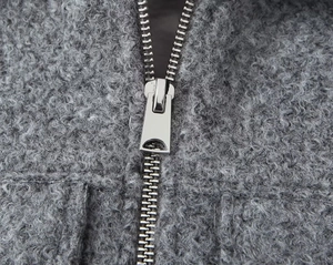 Detailed macro view of the silver metal zipper on a grey textured wool jacket fabric