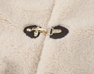 Detail of golden metal buckles on cream fleece jacket with brown leather accents