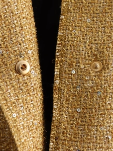 Detail of gold tweed fabric with metallic thread, sequins and round metal snap button