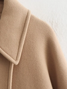 Detailed close-up of notch lapel and shoulder tailoring on camel wool coat with twill texture