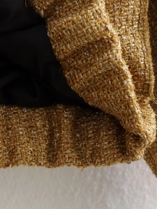 Macro detail of gold tweed fabric with metallic threads and sequin accents on jacket