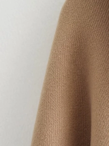 Macro shot of camel wool coat fabric showing fine diagonal weave texture and thick soft quality