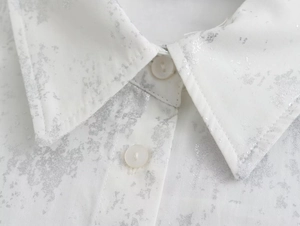 Detail of white shirt collar featuring silver metallic print and neat white buttons