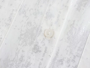 Macro detail of white shirt fabric with silver metallic coating and resin button