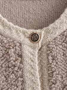 Close-up of beige bouclé knit cardigan with vintage gold-rimmed crest button detailing