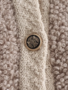Detailed close-up of premium bouclé knit fabric with an ornate gold heraldic button