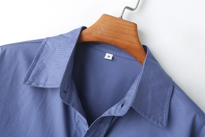 Détail du col d'une chemise bleue et texture du tissu avec étiquette S sur cintre en bois