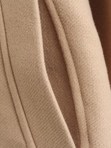Detailed close-up of camel wool coat fabric with high-quality twill weaving and pocket stitching