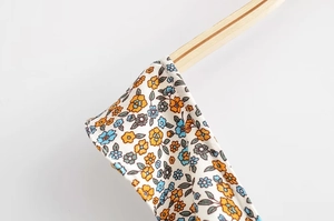 Detail of floral ruffle summer dress with orange and blue blooms on cream fabric