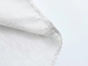 Detailed close-up of white fabric with silver marble texture and fine stitching on shirt hem