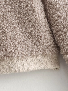 Detailed macro view of beige bouclé knit fabric with contrasting ribbed hem texture