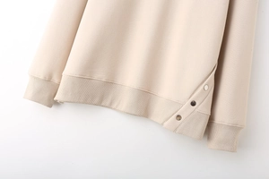 Detail of cream knit sweatshirt featuring side slit with three metallic snap buttons