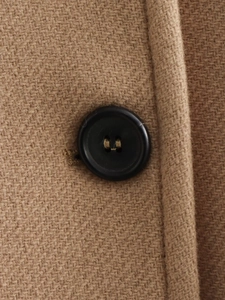 Macro shot of wool blend fabric texture with black resin button on a camel coat
