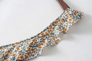 Detailed view of floral pattern chiffon fabric with ruffled edges on a wooden hanger