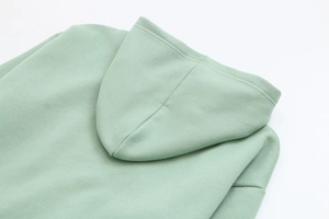 Detail view of high-density cotton fabric and double-stitched hood seams on light green hoodie