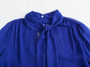 Close-up of royal blue chiffon blouse featuring an elegant pussy-bow tie and white button