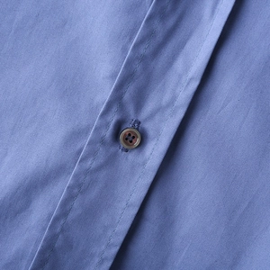Gros plan d'une chemise bleue style coupe-vent avec texture et détail de bouton marron