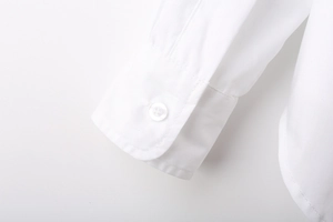 Detailed close-up of white long sleeve shirt showing buttoned cuff and curved side hem seam