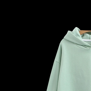 Detail of mint green cotton hoodie with white drawstrings on a wooden hanger