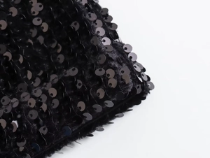 Dettaglio di paillettes nere su tessuto che mostra la trama e la finitura lucida