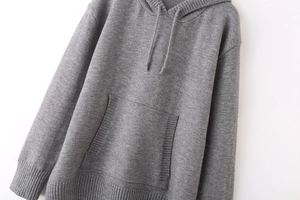 Detail of grey knitted hoodie showing kangaroo pocket, drawstring hood and ribbed cuffs