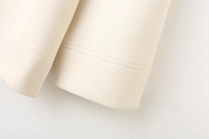 Detailed close-up of ribbed cuffs and twin-needle stitching on a cream white sweatshirt